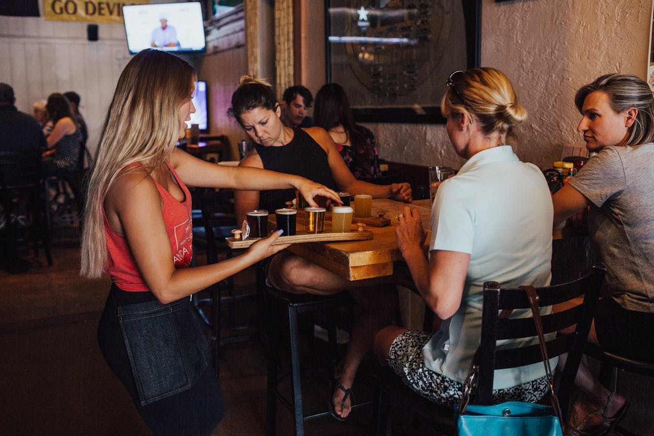 A group of women enjoying drinks served by a bartender in a cozy indoor bar environment.